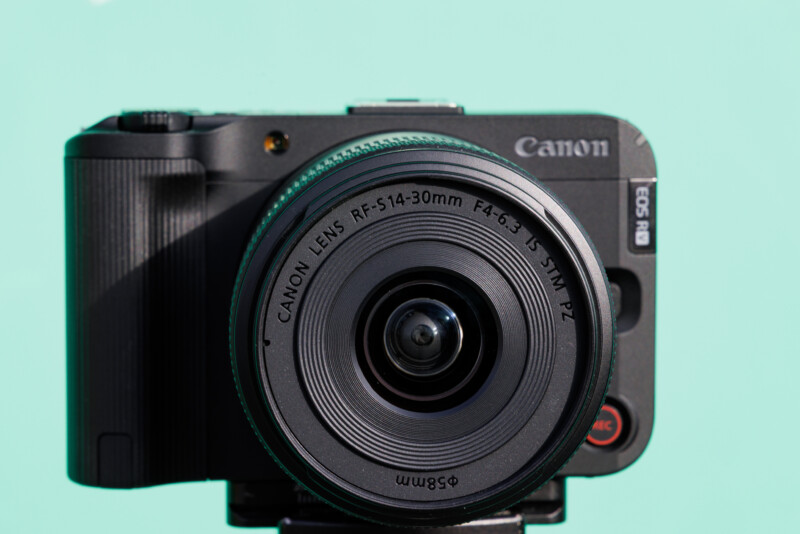 Front view of a Canon EOS R8 camera with a Canon RF 5.1-30mm lens on a turquoise background.