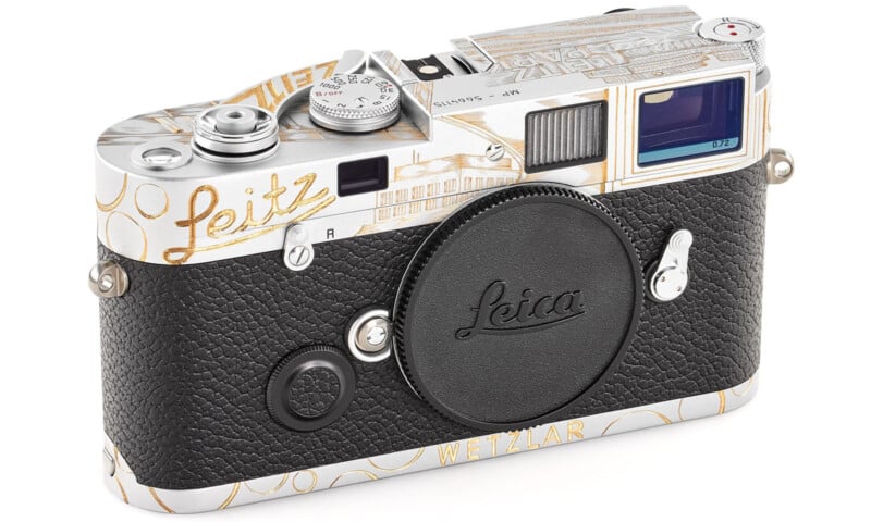 A limited edition Leica camera with a black textured grip, silver top, gold accents, and "Leitz" written in gold script. The lens mount cap and "WETZLAR" are visible on the front.