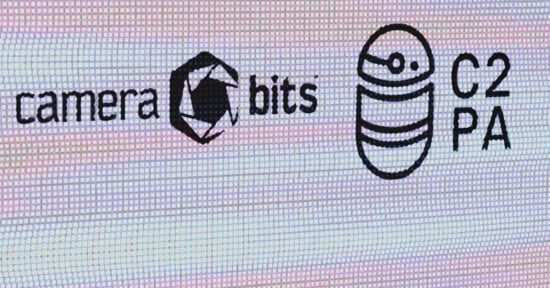 A digital screen displays logos, including the Camera Bits logo with a stylized camera aperture icon, and the C2PA logo featuring a circular design with horizontal lines and a dot. The words "camera bits" and "C2PA" are written next to their respective logos.