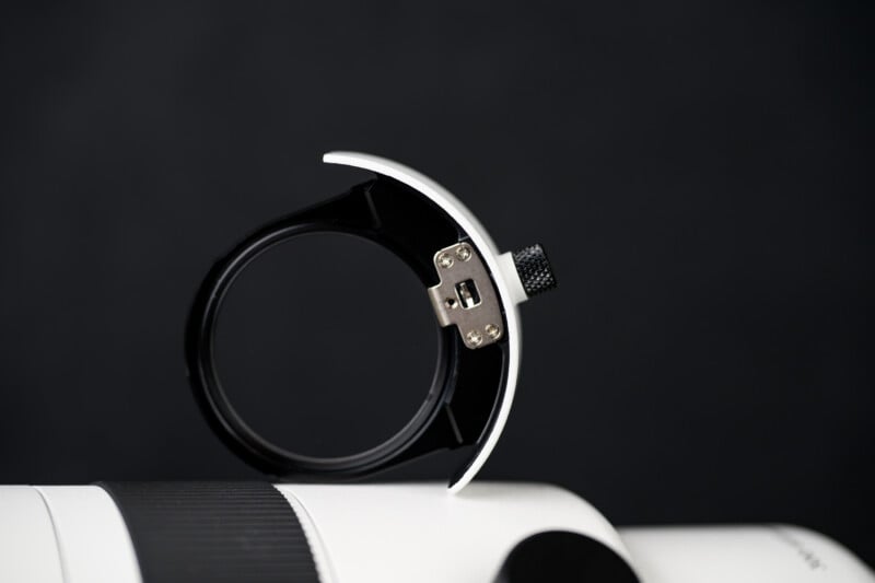 Close-up of a black and white camera lens collar mount against a dark, blurred background, showing a metal tightening screw and textured grip.