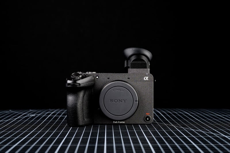 A Sony full-frame mirrorless camera with a body cap and electronic viewfinder sits on a grid-patterned surface against a black background.