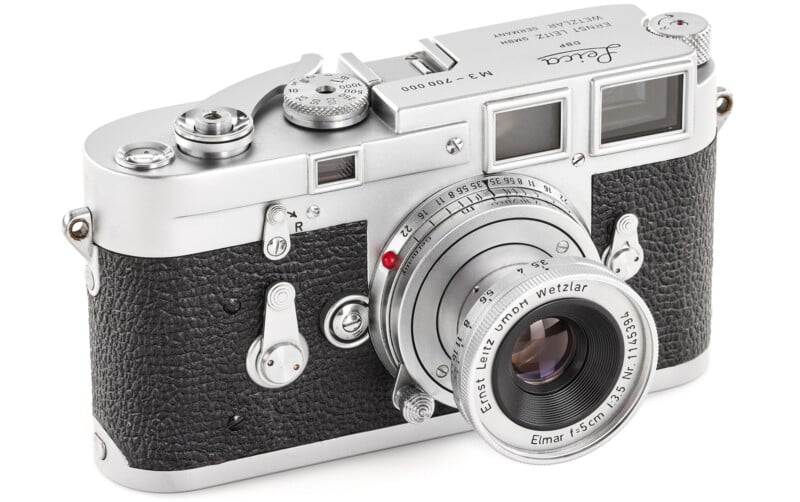 A vintage silver and black Leica film camera with a textured grip and an Ernst Leitz Wetzlar Elmar 50mm f/3.5 lens, resting on a white surface.