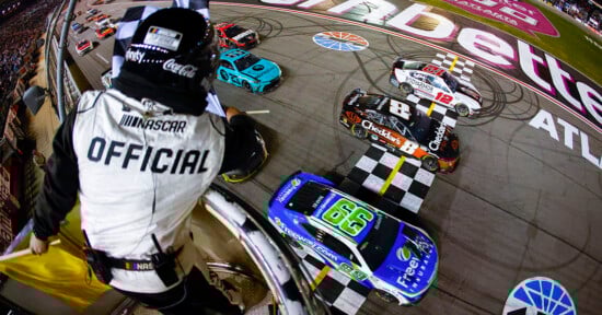 A NASCAR official in the foreground waves the checkered flag as Daniel Suarez beats Kyle Bush and Ryan Blaney across the finish line.