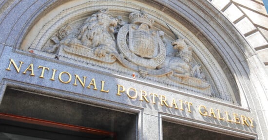 Entrance of the National Portrait Gallery, featuring ornate stone carvings of the Royal Coat of Arms and gold letters spelling out the gallery's name above the doorway.