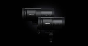 Two black Profoto studio lights are positioned side by side against a dark background, showcasing their sleek, cylindrical design and control panels.