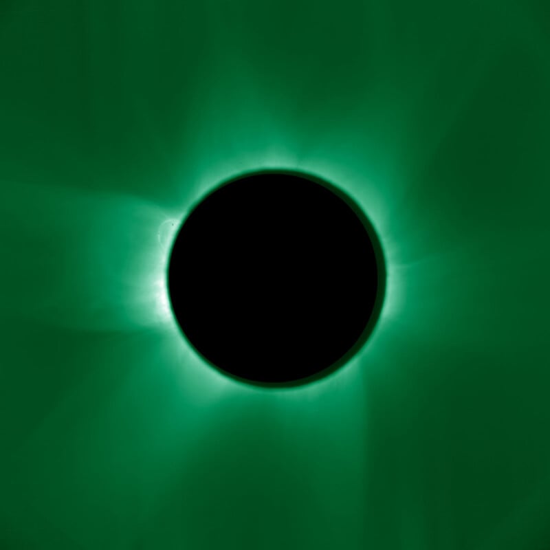 A black circle, representing the moon, blocks the sun, creating a solar eclipse with a vivid green glowing corona radiating around the dark center.