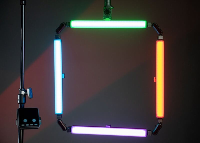 Four LED light bars in green, red, purple, and blue form a square shape, mounted on stands against a dark background. A control panel and a camera are also visible near the structure.