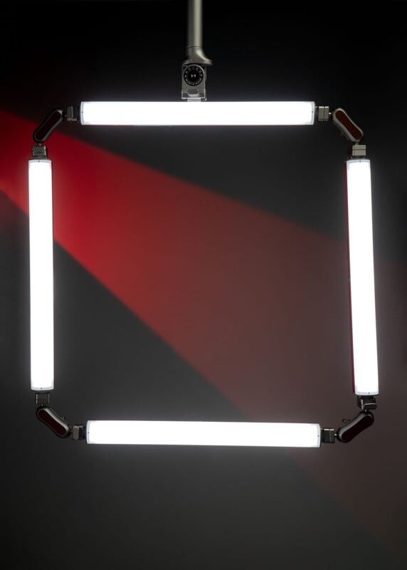 Four bright LED light bars form a square suspended in front of a dark background, with a red beam of light crossing diagonally behind the square.