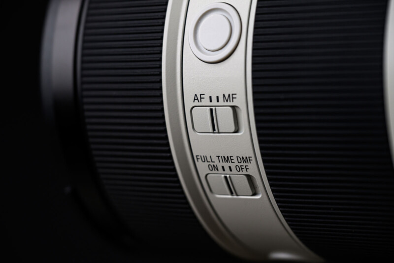 Close-up of a camera lens showing switches for autofocus/manual focus (AF/MF) and full-time direct manual focus (DMF) with ON and OFF positions, set against a black background.