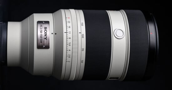 Close-up of a Sony FE 2.8/70-200 GM interchangeable camera lens with a white barrel, black focus and zoom rings, and a metal nameplate, set against a black background.