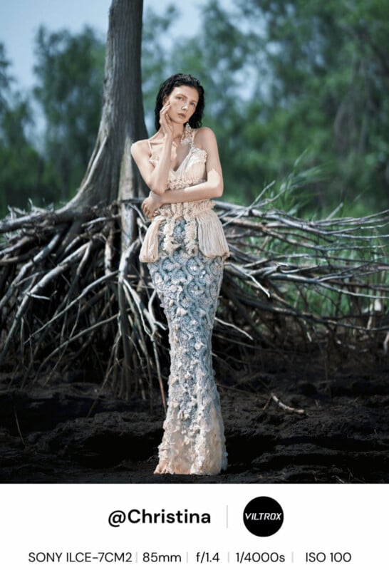 A woman in a textured, light-colored dress stands in front of exposed tree roots and greenery, posing with one hand on her head and one on her neck. Camera settings and credits are shown at the bottom of the image.