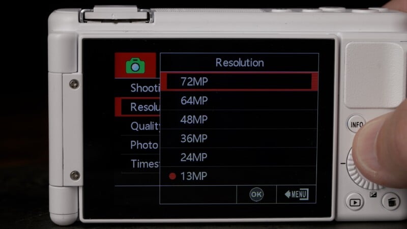 The back screen of a digital camera displays a resolution settings menu, with options ranging from 13MP to 72MP. A hand is adjusting settings using the control dial on the right side of the camera.